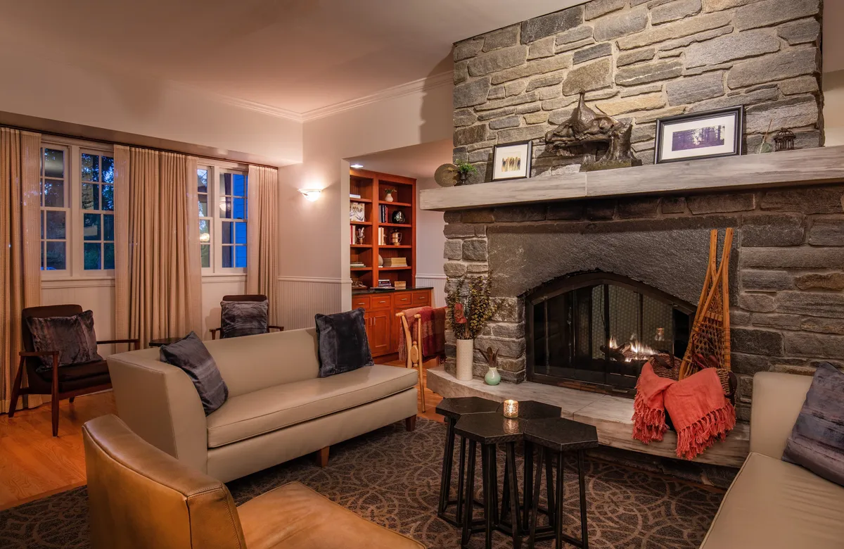A welcoming interior scene centers around a classic stone fireplace flanked by plush sofas and curated decorative items on the mantel. The arrangement invites relaxation, intimate conversation, and quiet evenings by the fire—underscoring a sense of timeless elegance and comfort.
